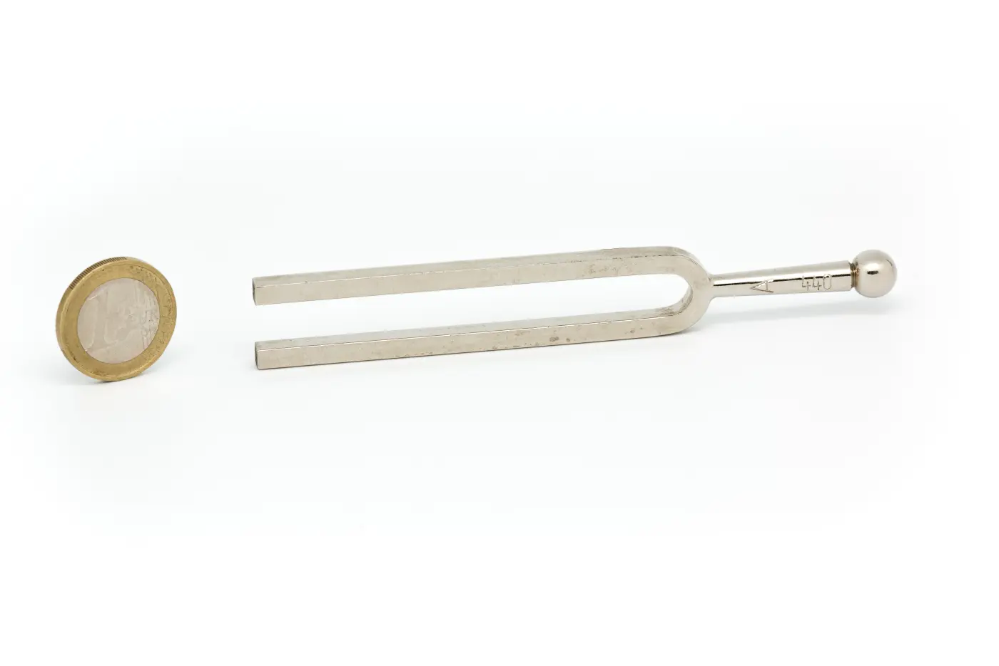 Chrome tuning fork with square prongs stamped 440 Hz lying on a plain surface