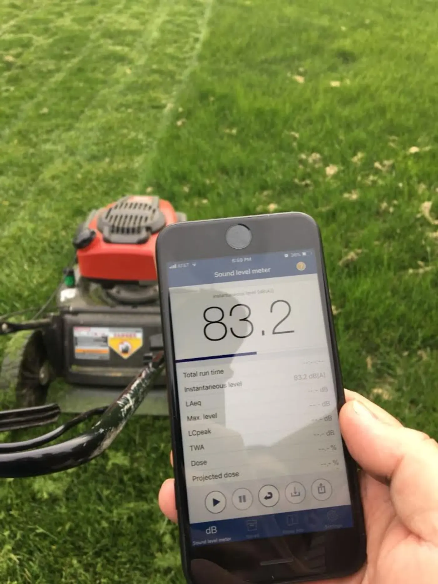 Phone screen showing a sound level meter app reading 83 decibels next to a lawn mower