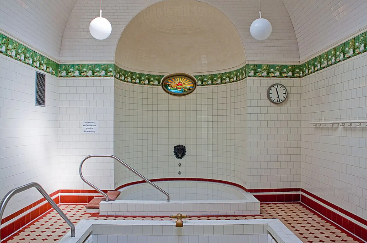 A small tiled cold plunge pool with metal handrails in a historic bathhouse