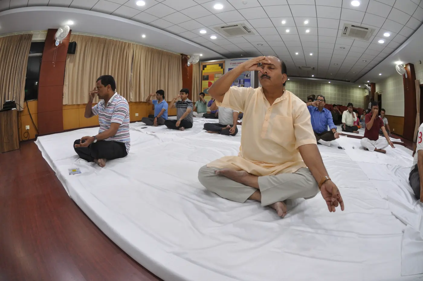 Group of people sitting cross-legged on white mats practising alternate-nostril breathing