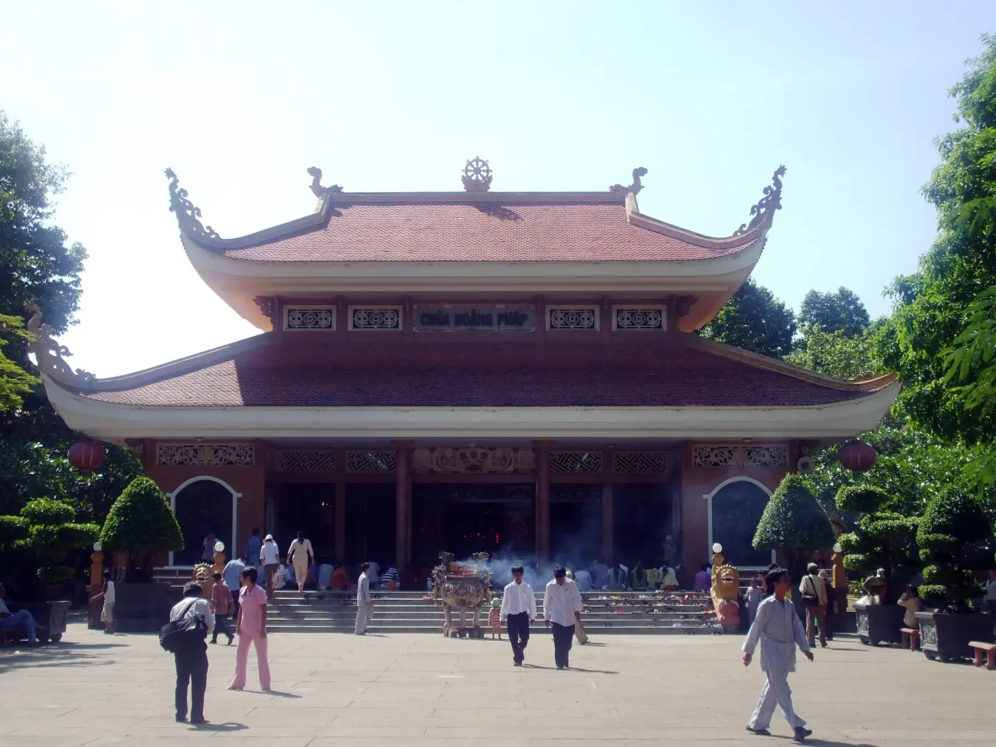 Sala principal de la pagoda Hoằng Pháp en Hóc Môn, con tejados curvos de tejas y visitantes en el patio
