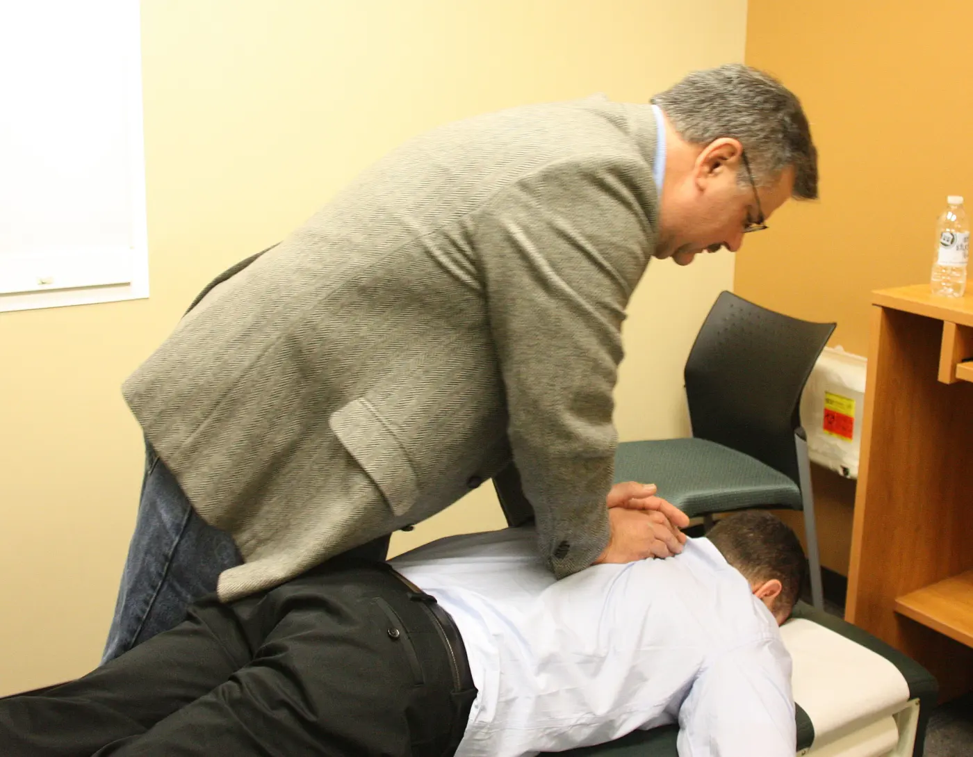 A practitioner leaning over a patient lying face down on a treatment table, hands placed on the upper back