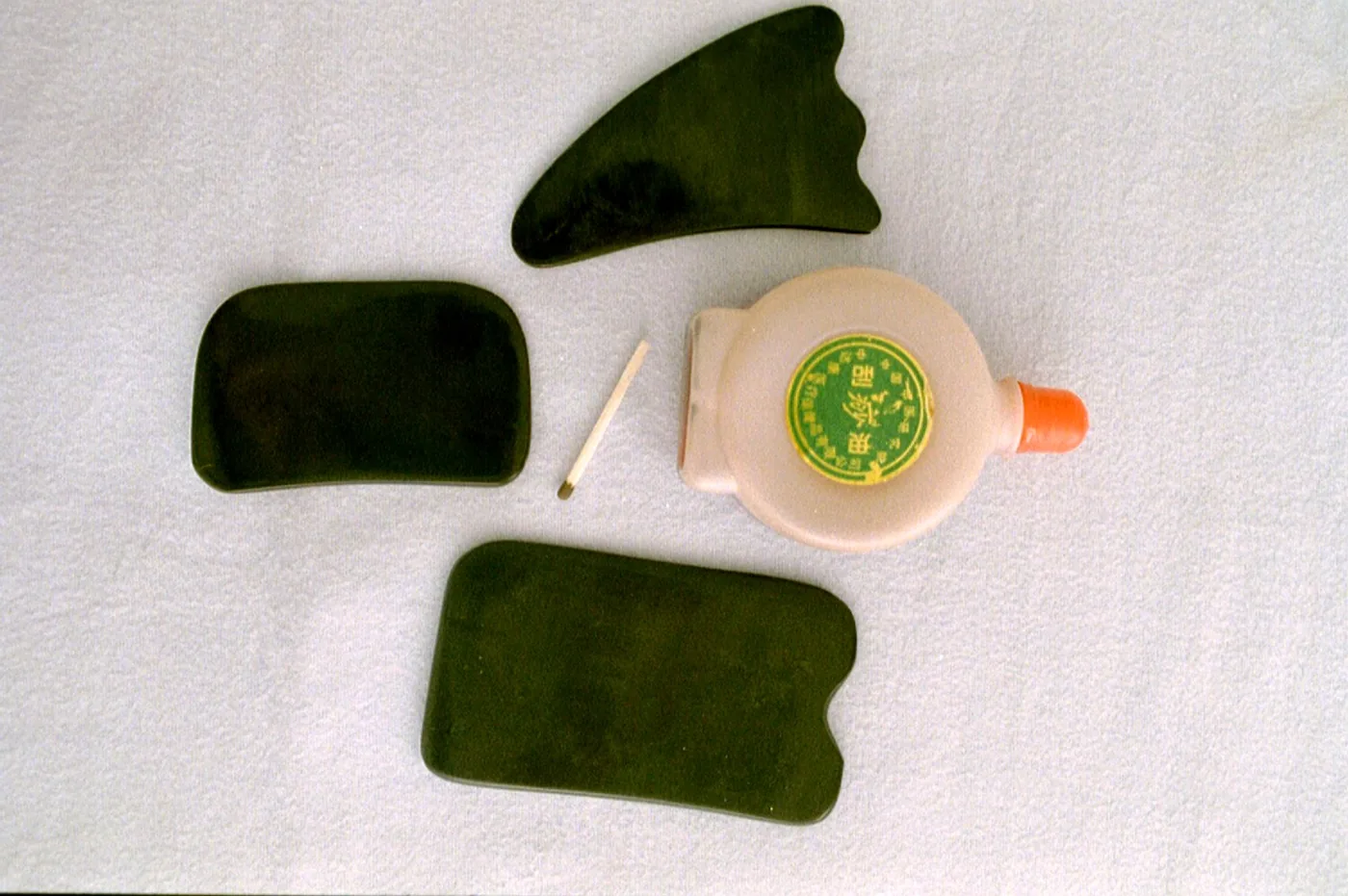 Three dark smooth scraping boards in different shapes and a small plastic bottle of oil laid out on a light cloth