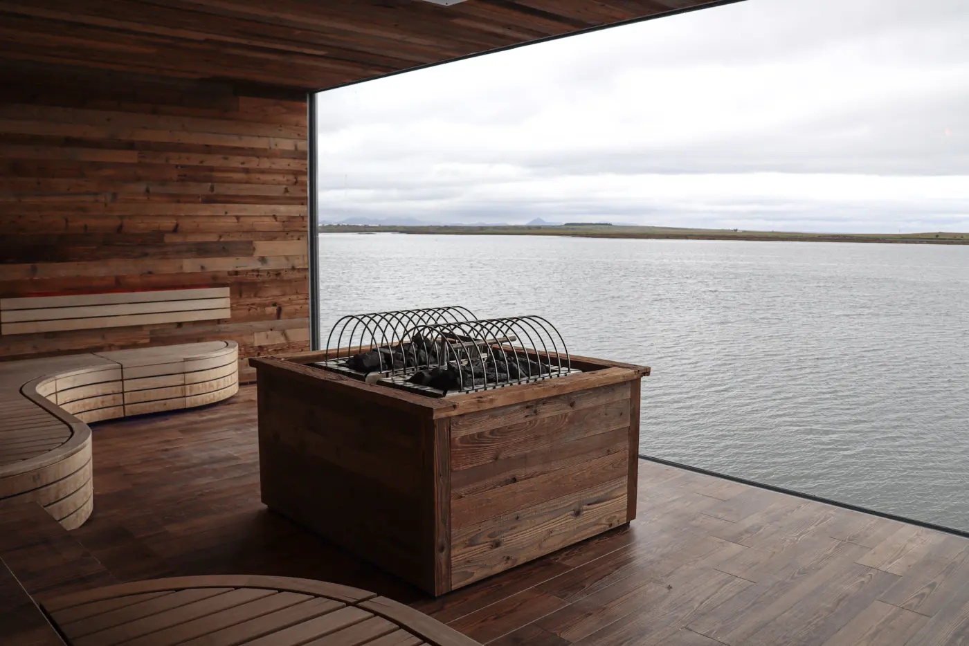 Wooden sauna with a stone heater and a large window looking out over calm grey sea