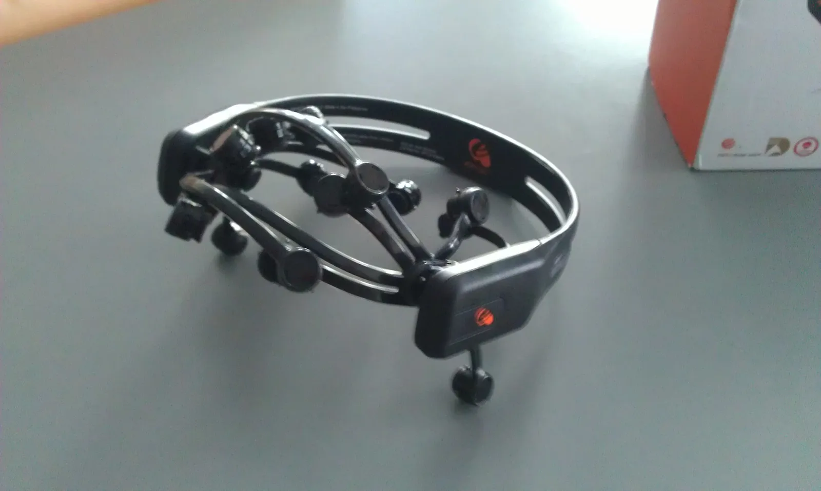 Black wireless EEG headset with multiple sensor arms resting on a grey table.