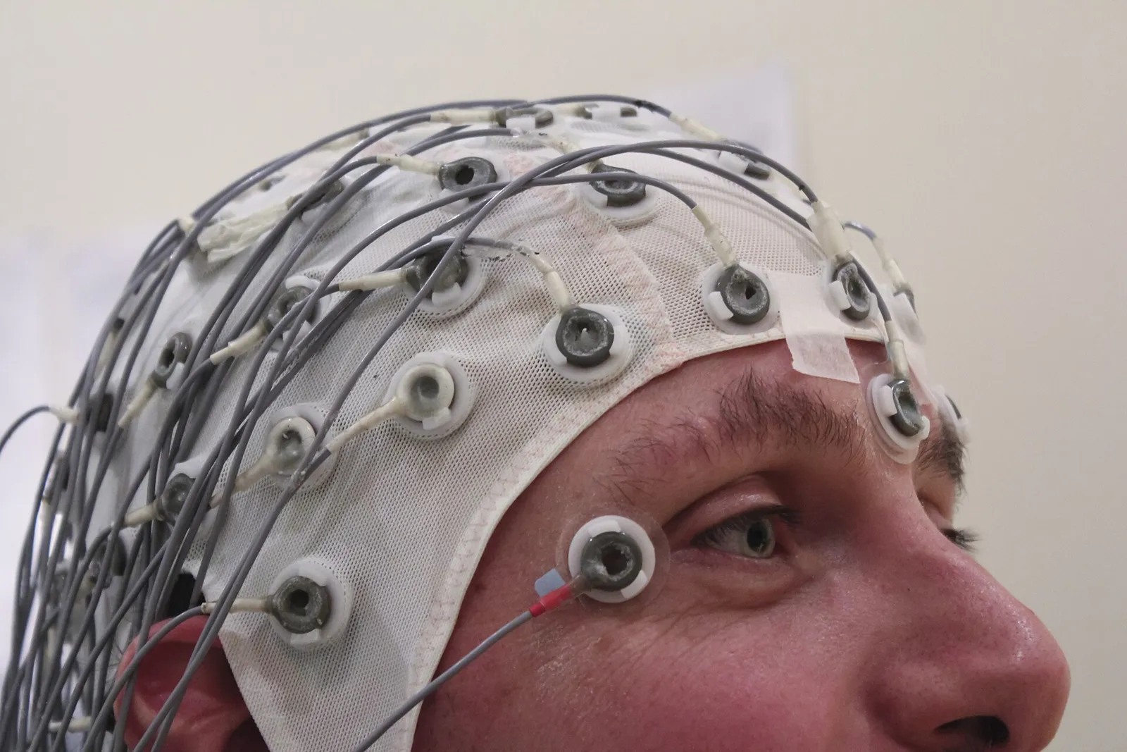 Close-up of a man wearing an EEG cap covered in electrodes and wires
