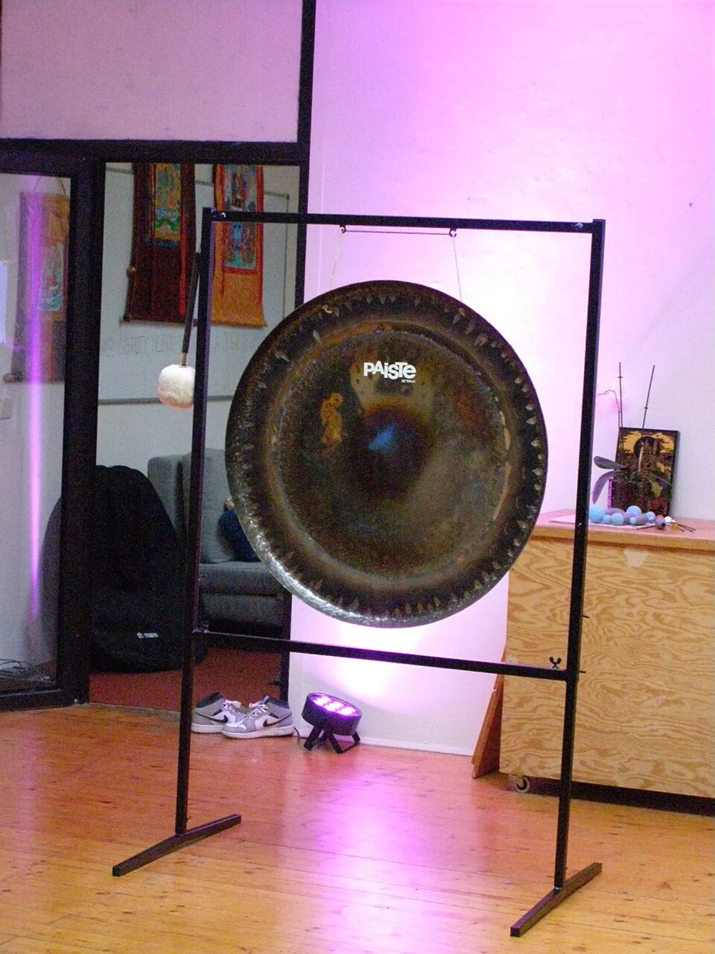 Un gran gong sinfónico oscuro colgado de un marco de metal negro en un estudio con luz suave y suelo de madera