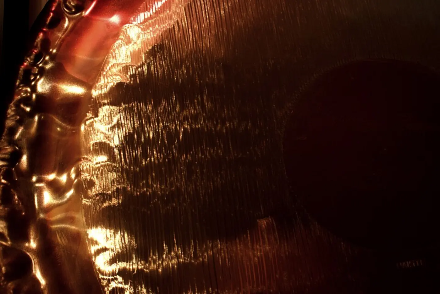 Primer plano de la superficie martillada color bronce y el borde de un gong sinfónico con luz cálida y tenue