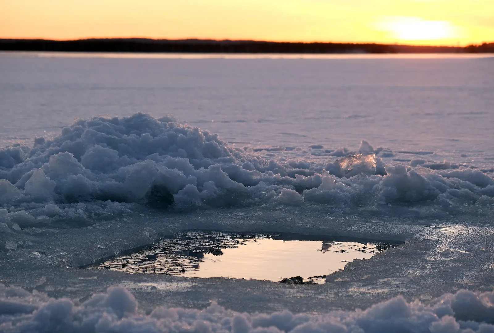 Square ice hole in a frozen lake glowing with sunset light