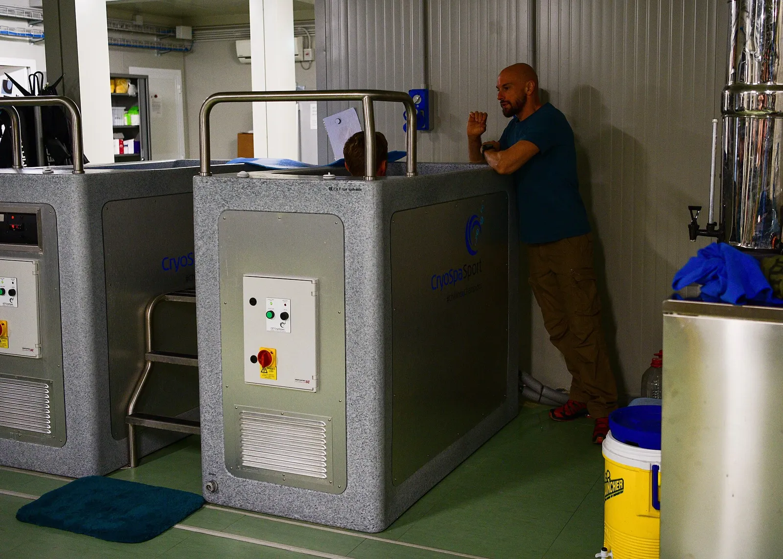 Two cold-water immersion tubs with a person sitting in one while an instructor watches