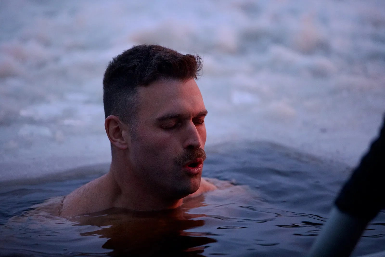 Man up to his shoulders in icy water, eyes half closed, breathing slowly