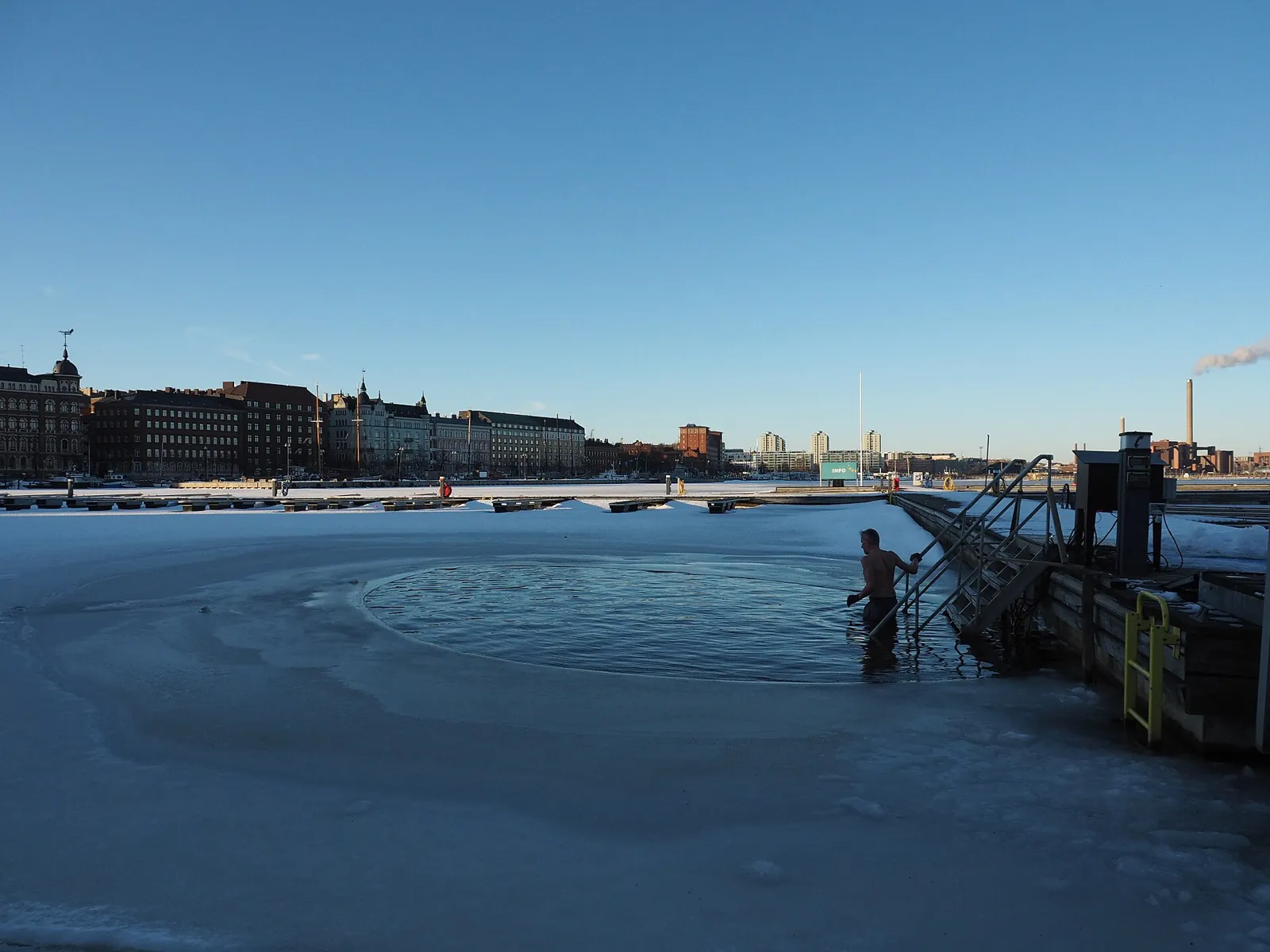Winter swimmer climbing down a ladder into icy sea water with the Helsinki skyline behind