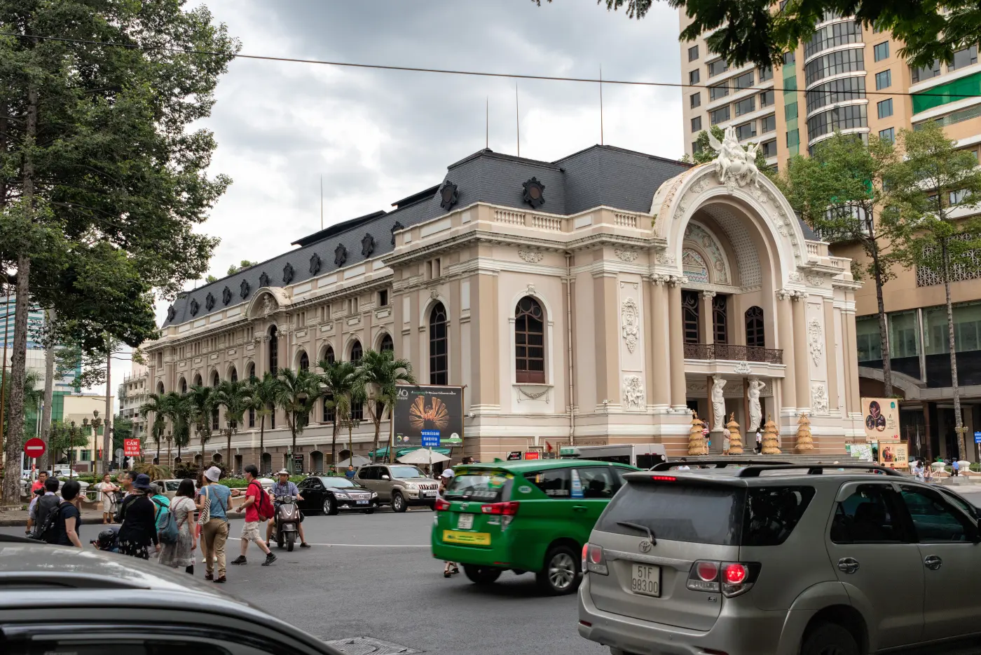 Mặt tiền màu kem của Nhà hát Thành phố Hồ Chí Minh, phía trước là taxi và dòng xe cộ