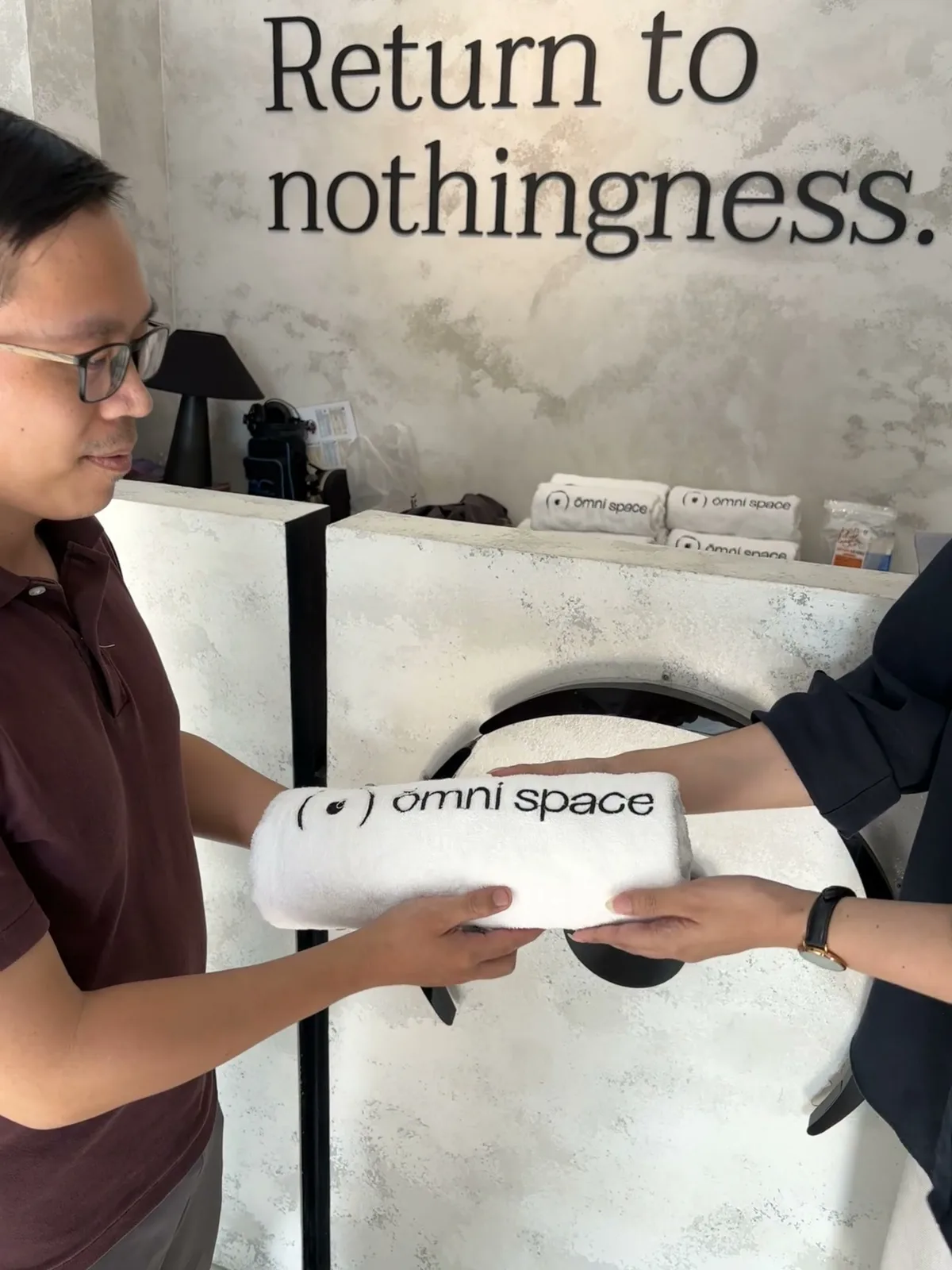 Ōmni Space staff member handing a folded towel to a guest at check-in