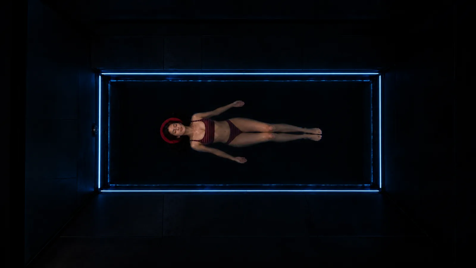 A woman floating small in the middle of a dark float pool at Ōmni Space as the lights dim