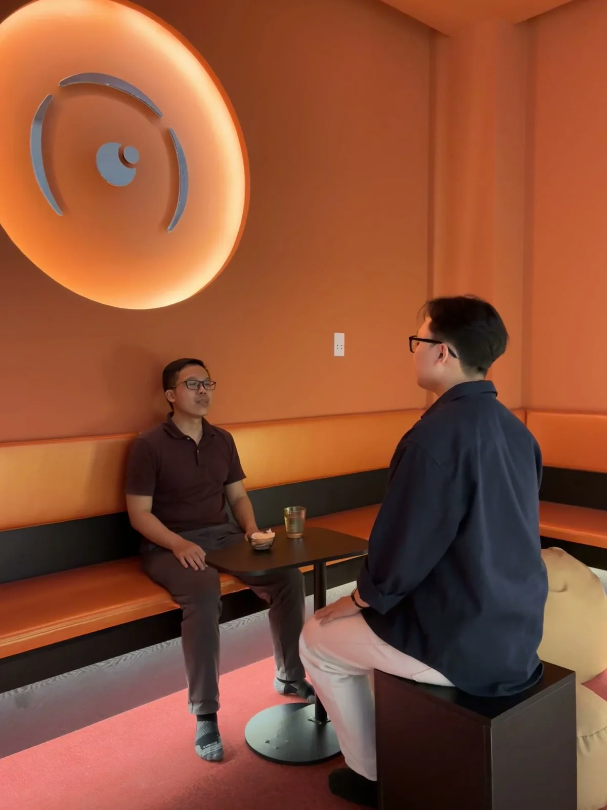 Two people talking in the orange lounge at Ōmni Space