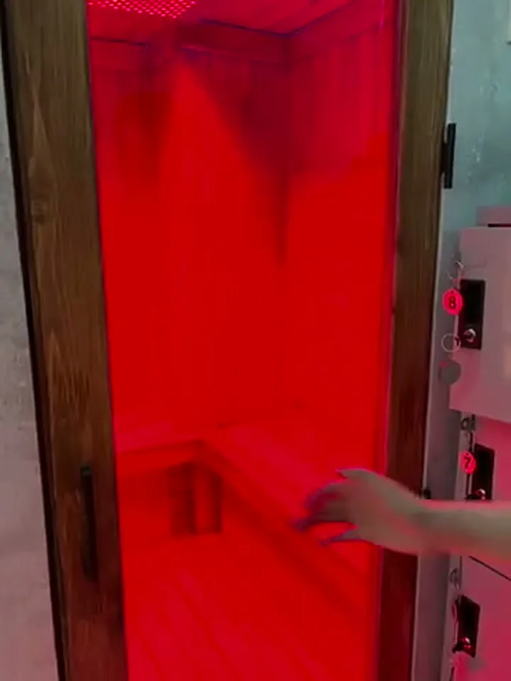 Interior de la sauna de infrarrojos y luz roja de Ōmni Space, con bancos de madera iluminados en rojo