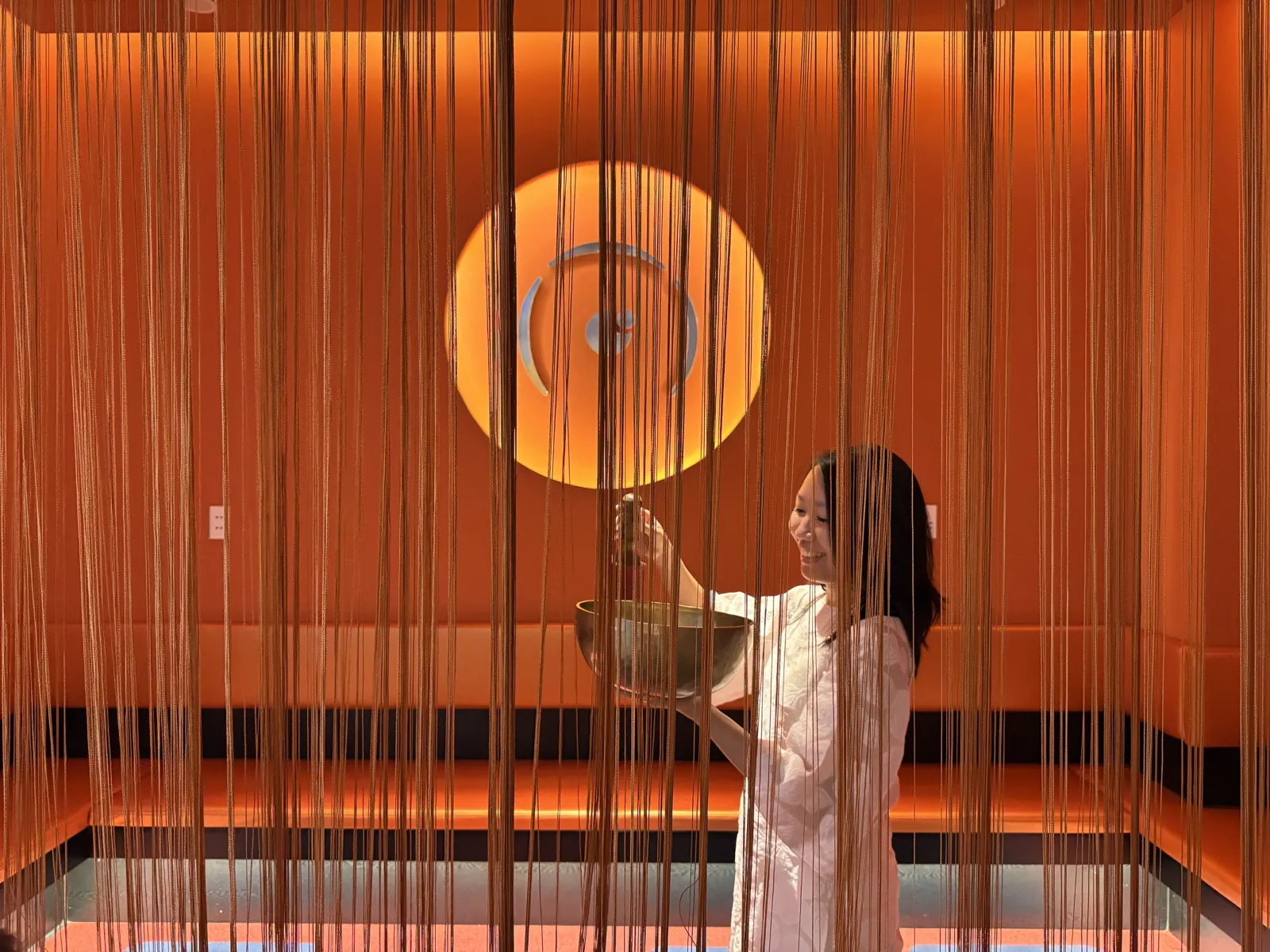 A sound practitioner playing a singing bowl behind a string curtain