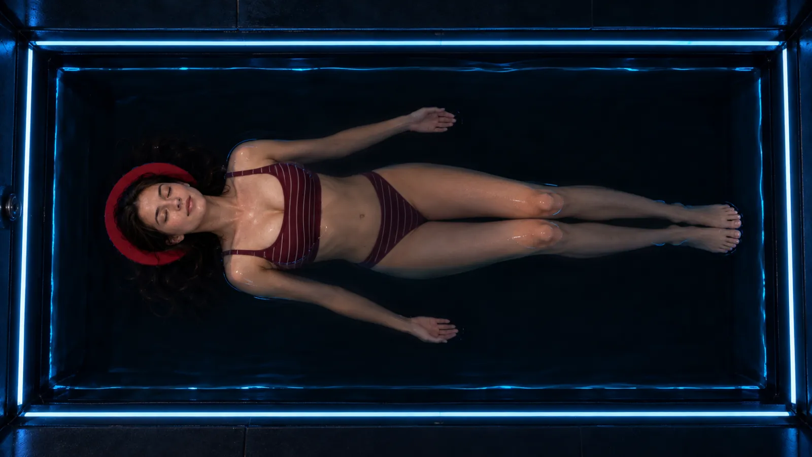 A woman floating on her back in the Ōmni float pool, seen from above, head resting on a float halo