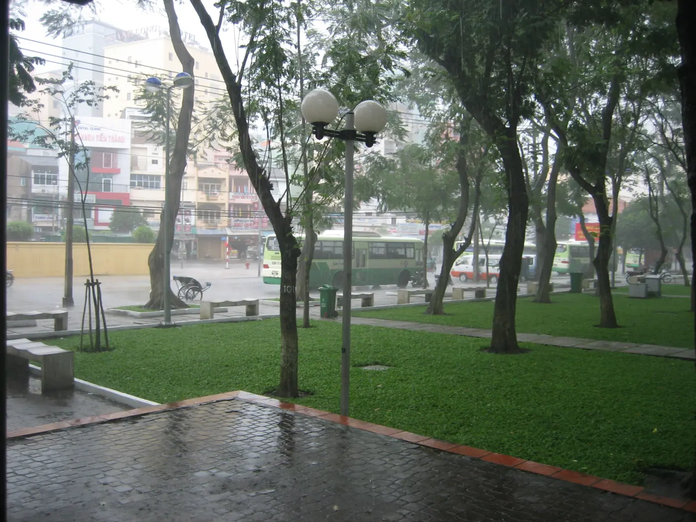 Mưa rơi trên một công viên yên tĩnh ở Sài Gòn với hàng cây, cột đèn và lối đi ướt