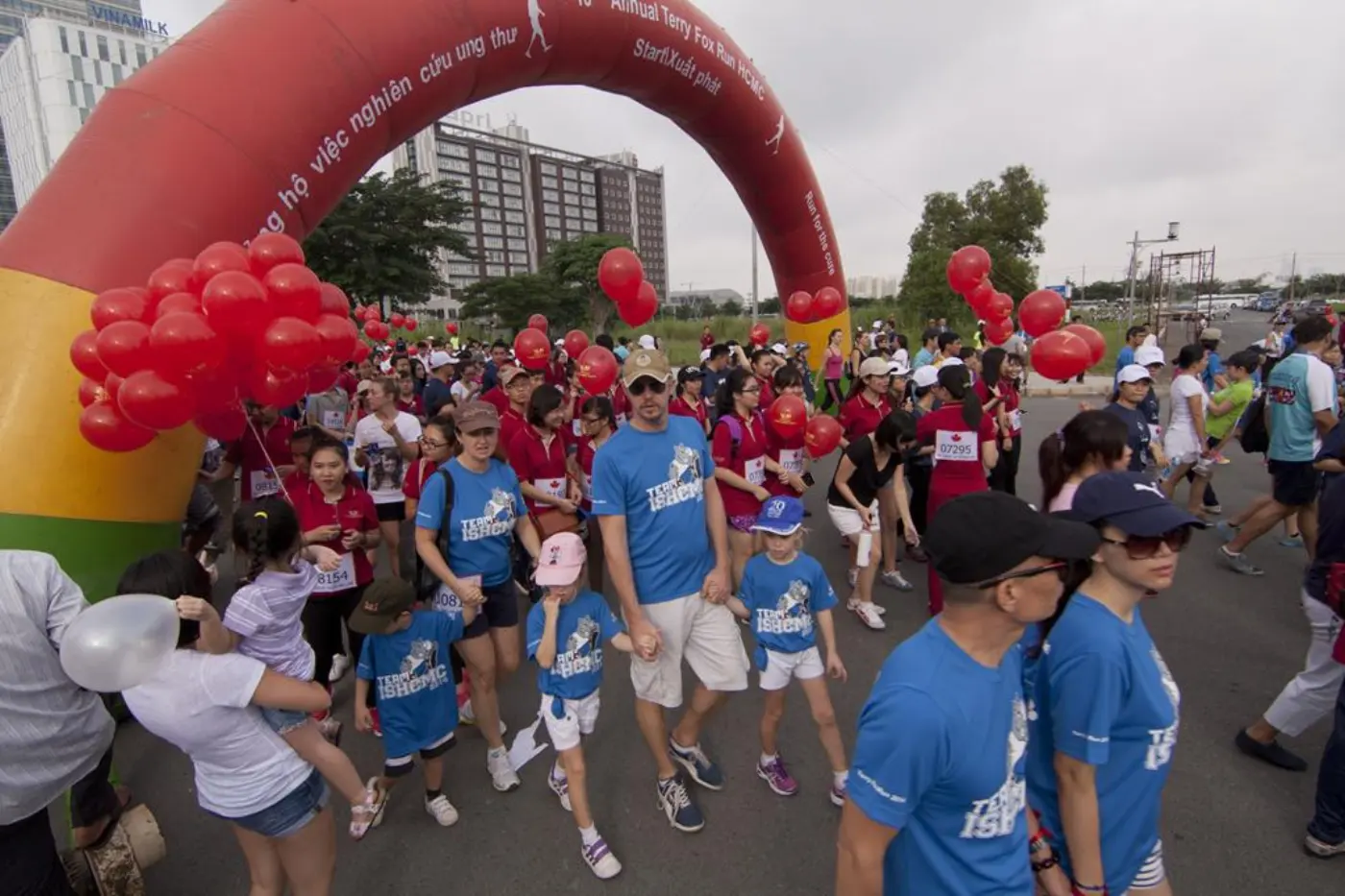 A crowd of runners and walkers in blue T-shirts setting off under an inflatable arch at a charity run in Ho Chi Minh City
