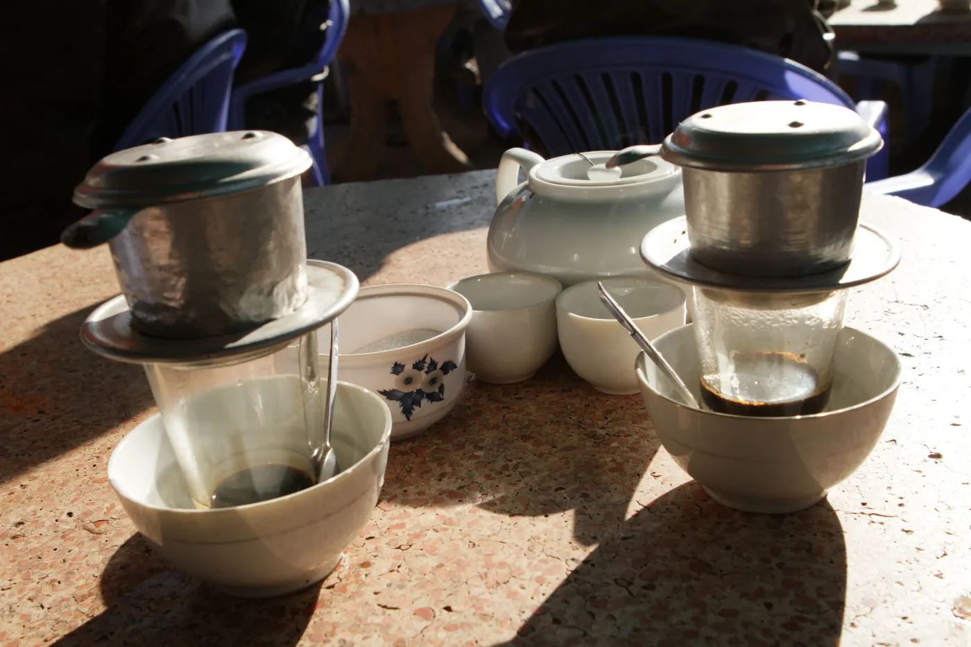 Two Vietnamese phin filters dripping coffee into cups set in bowls of hot water on a café table