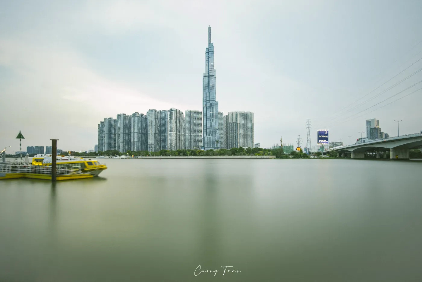 Yellow water bus on the calm Saigon River with Landmark 81 and towers behind