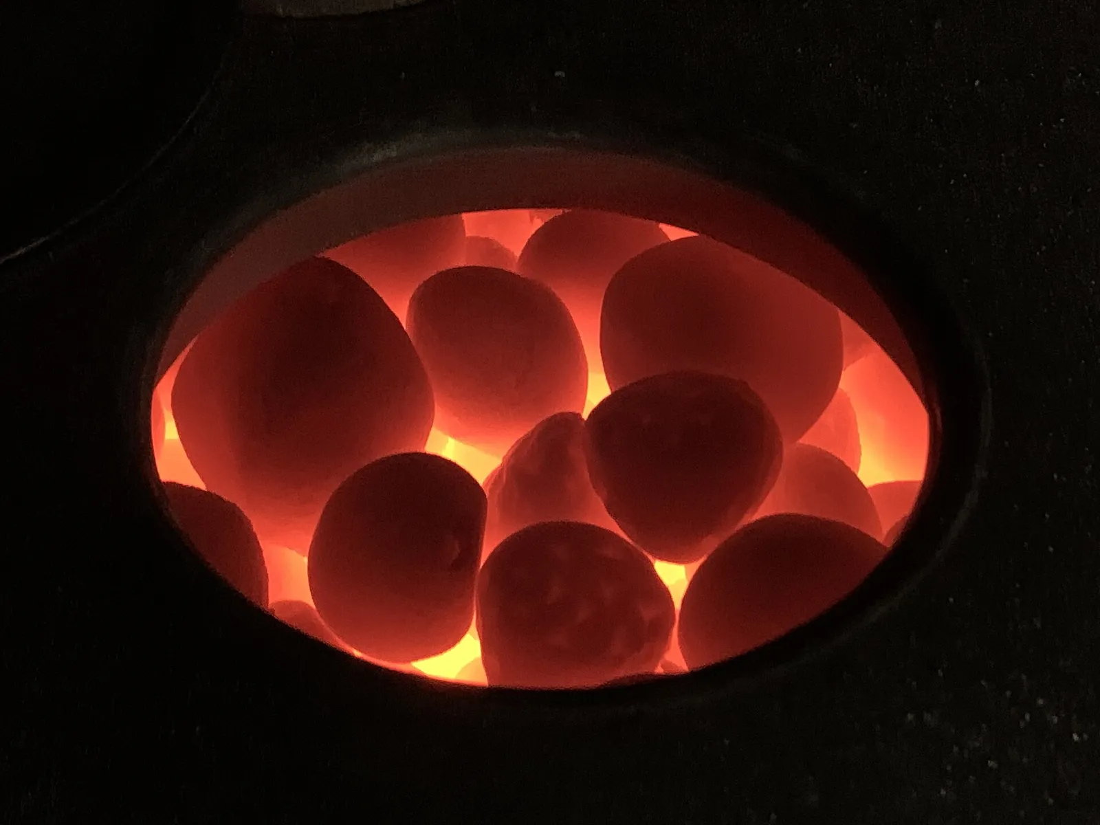Close-up of red-hot rounded stones glowing inside the open stone compartment of a sauna stove.
