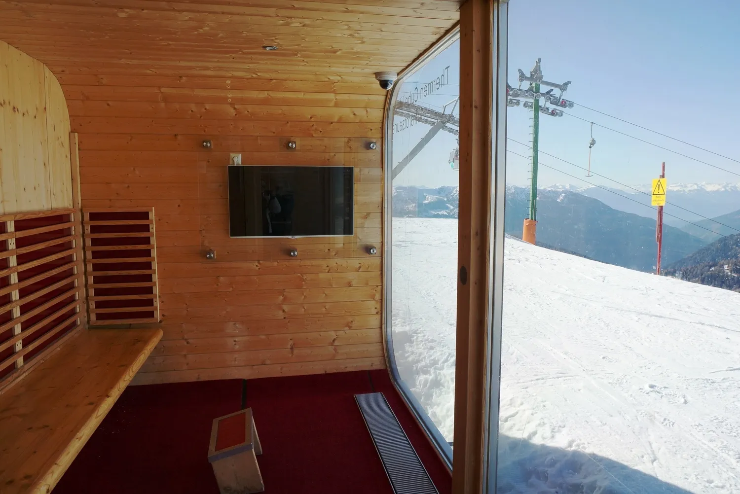 Wooden infrared sauna cabin with a large window over a snowy ski slope