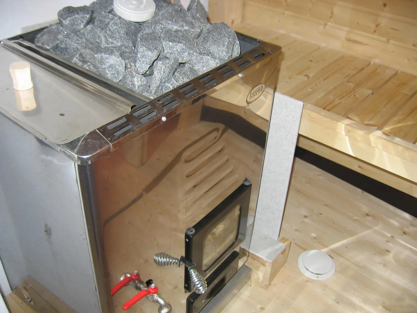 Metal Finnish sauna stove topped with sauna stones beside wooden benches