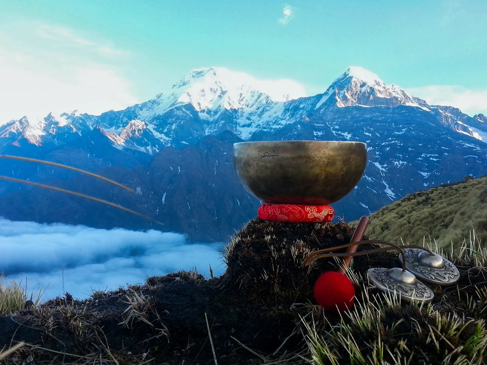 Bronze singing bowl on a red cushion with snowy Himalayan peaks behind