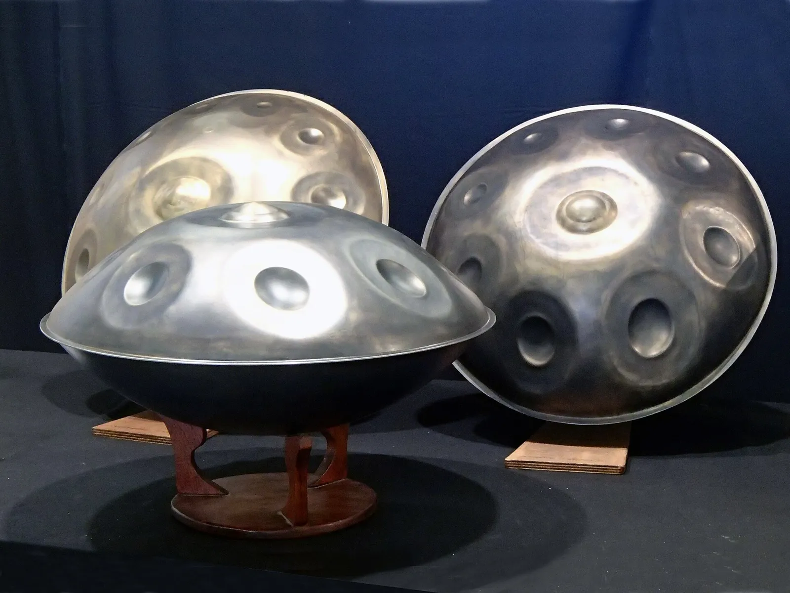 Three steel handpans on wooden stands against a dark background