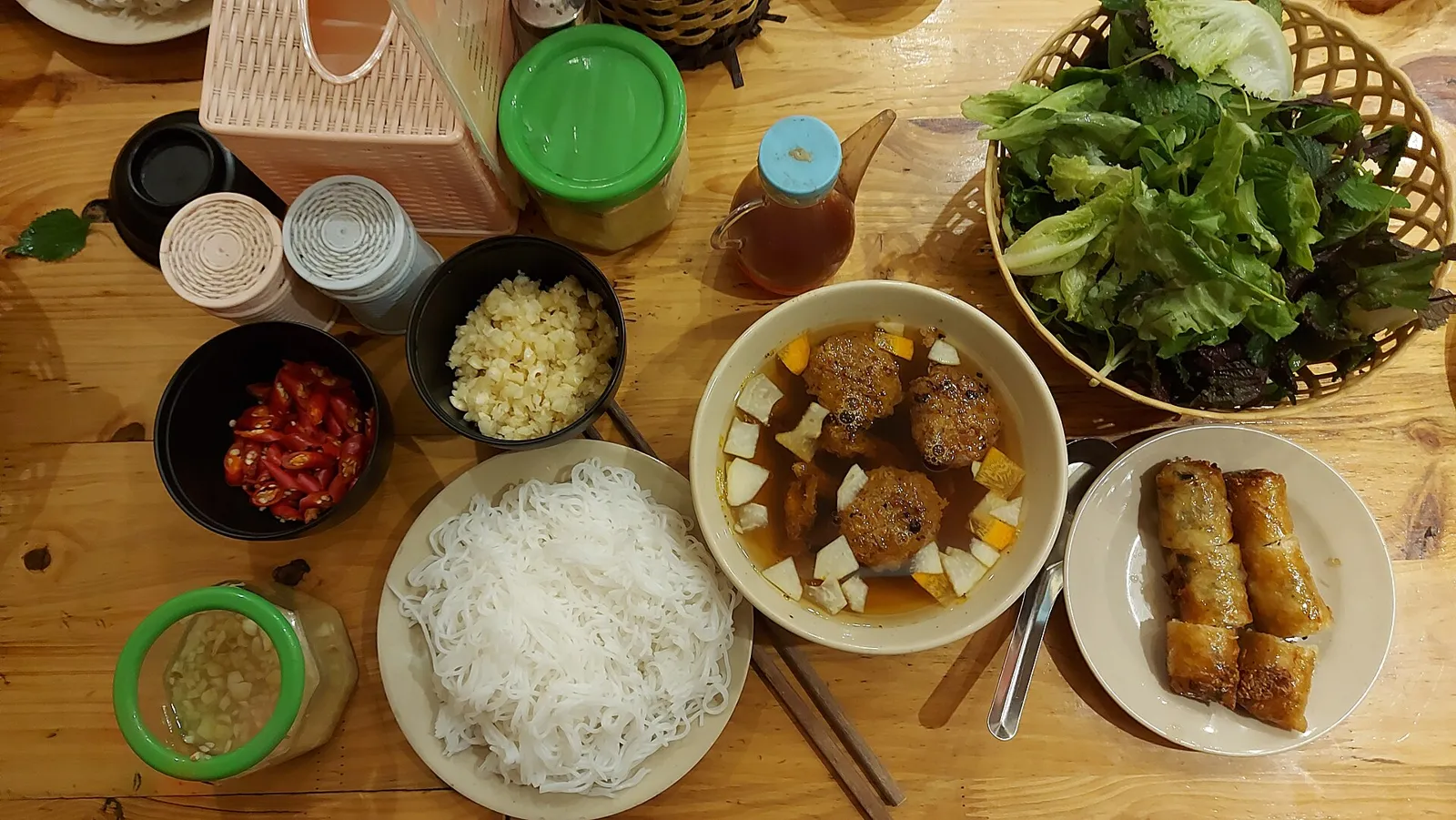 Vista cenital de bún chả: fideos, cerdo a la parrilla en caldo para mojar, hierbas y rollitos fritos