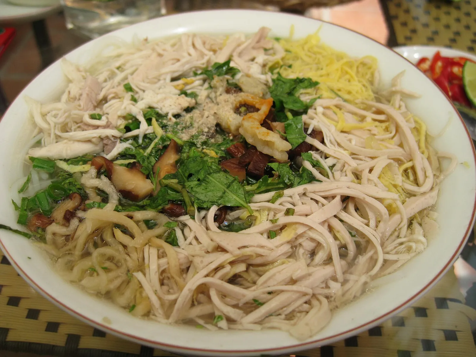 Bún thang con fideos de arroz, pollo desmenuzado, tiras de tortilla y hierbas