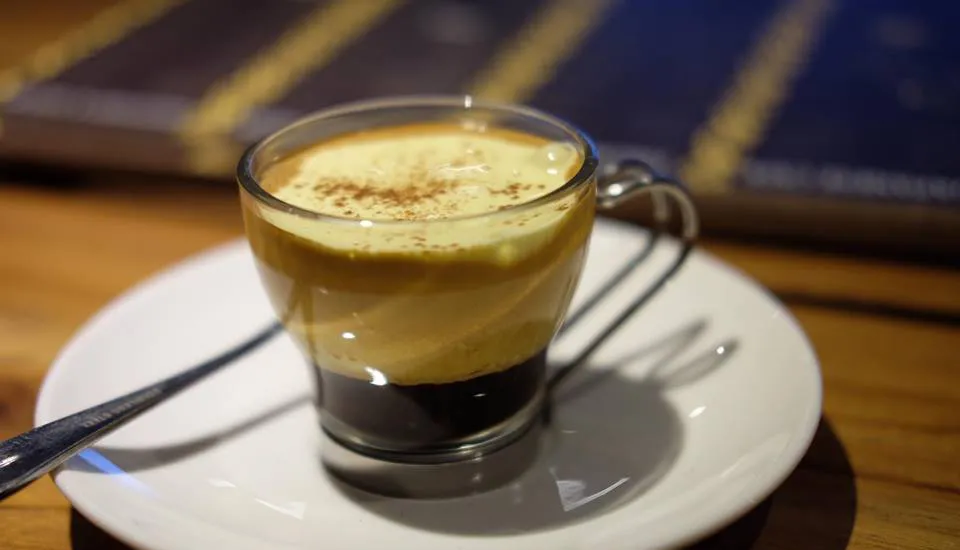 Café con espuma cremosa espolvoreada con cacao sobre un platillo blanco